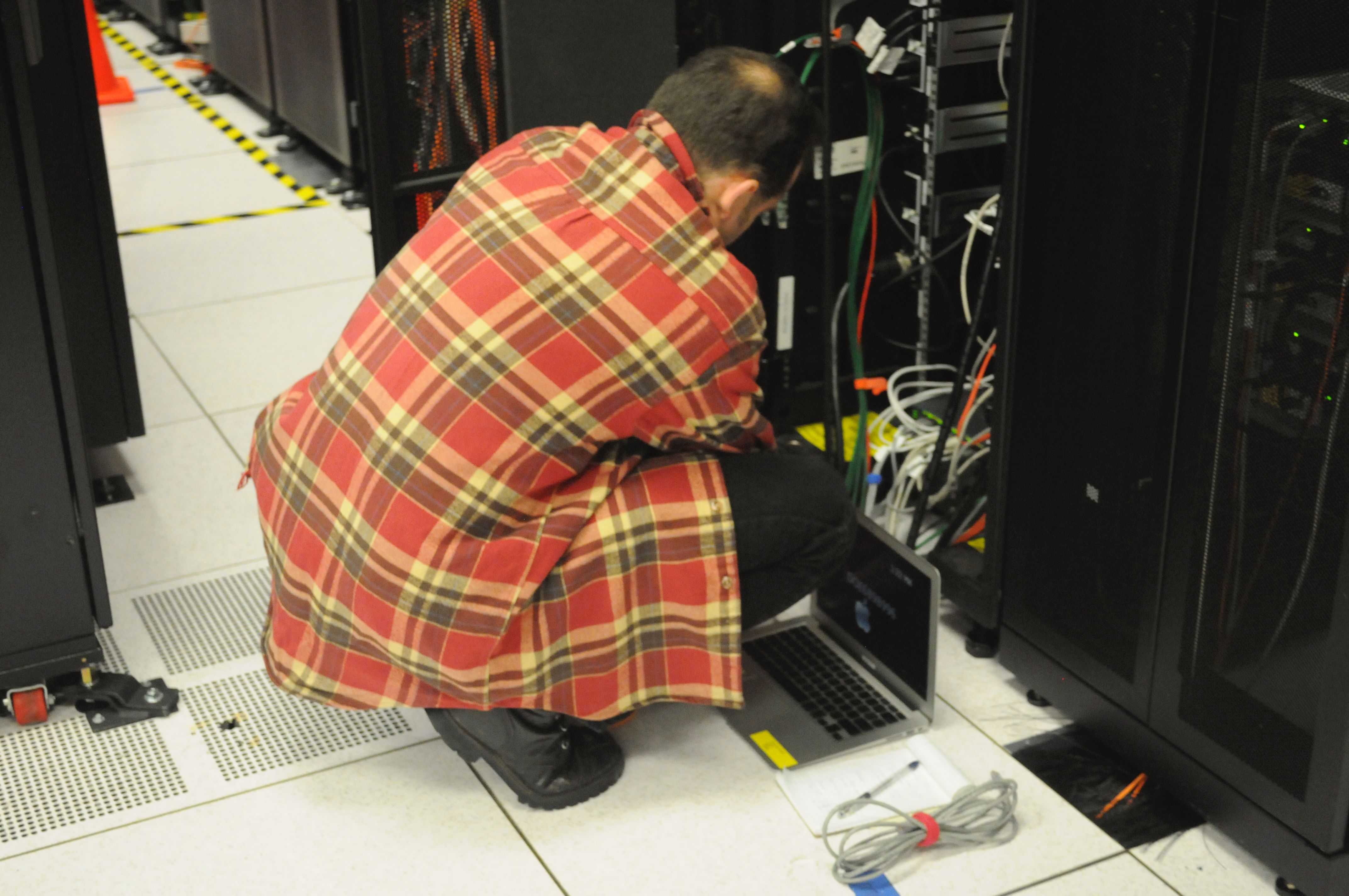 Technician working on server racks with a laptop, representing production agent infrastructure